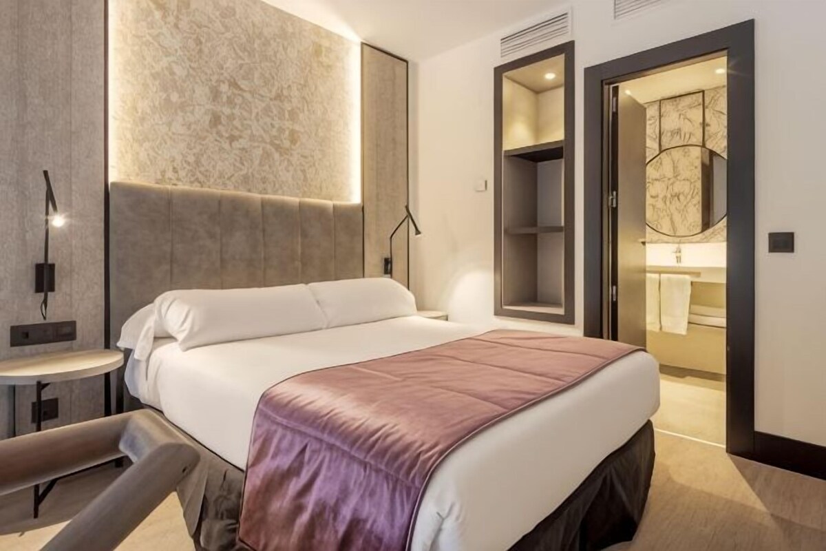 A modern hotel room with a large bed, bedside tables, a desk, and a walk-in closet.