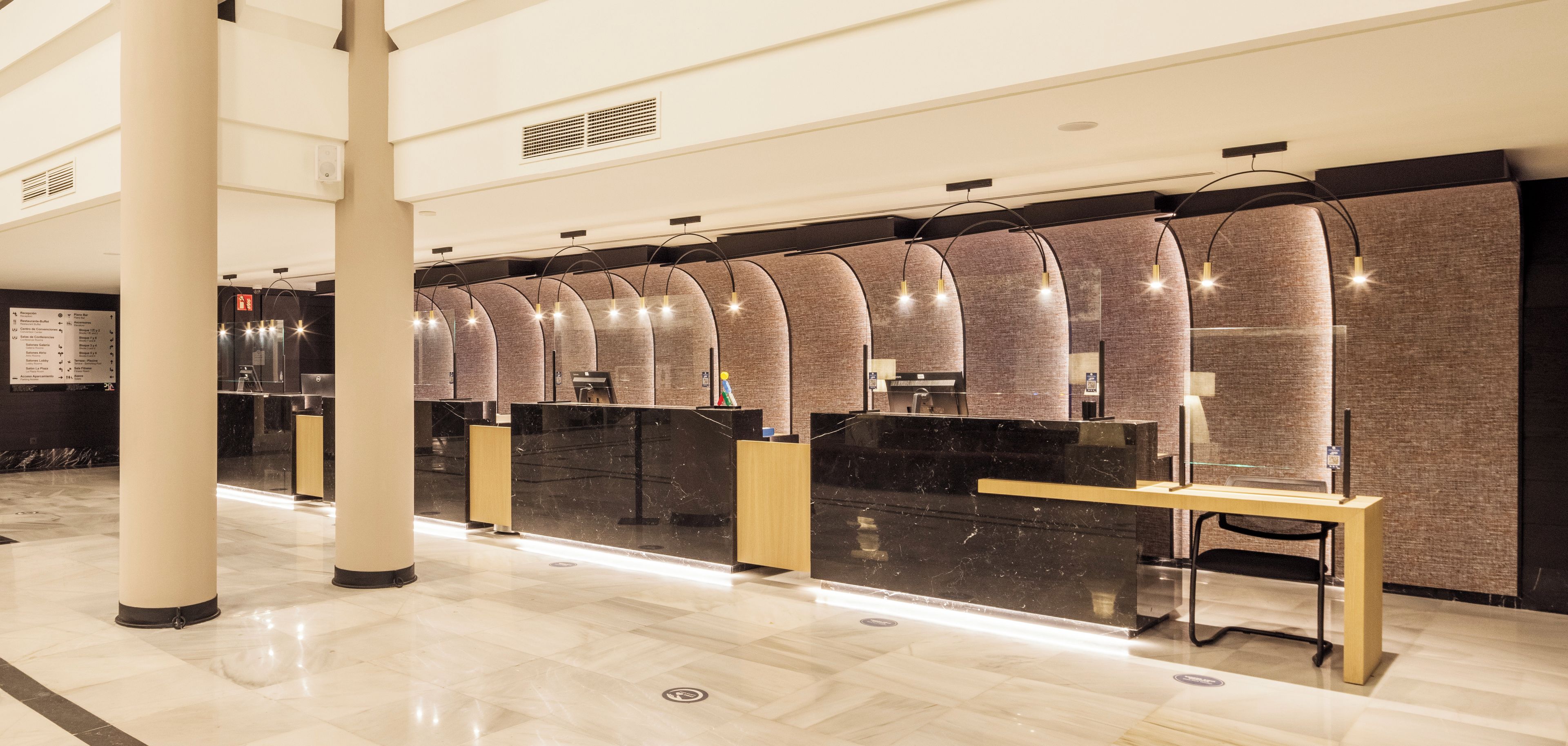 Zona de recepción de hotel con una larga barra de mostrador, estaciones de servicio individuales y suelo de mármol.