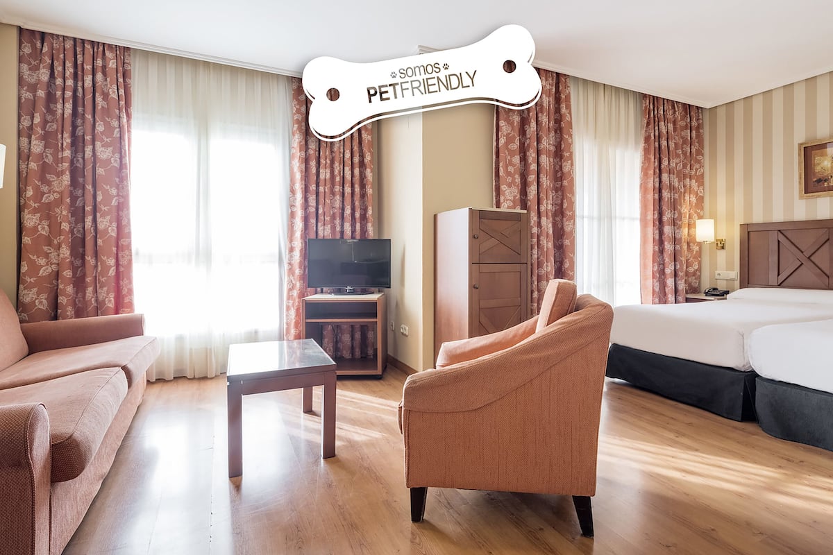 Een hotelkamer met een bank, fauteuil, bed, televisie en bureau.