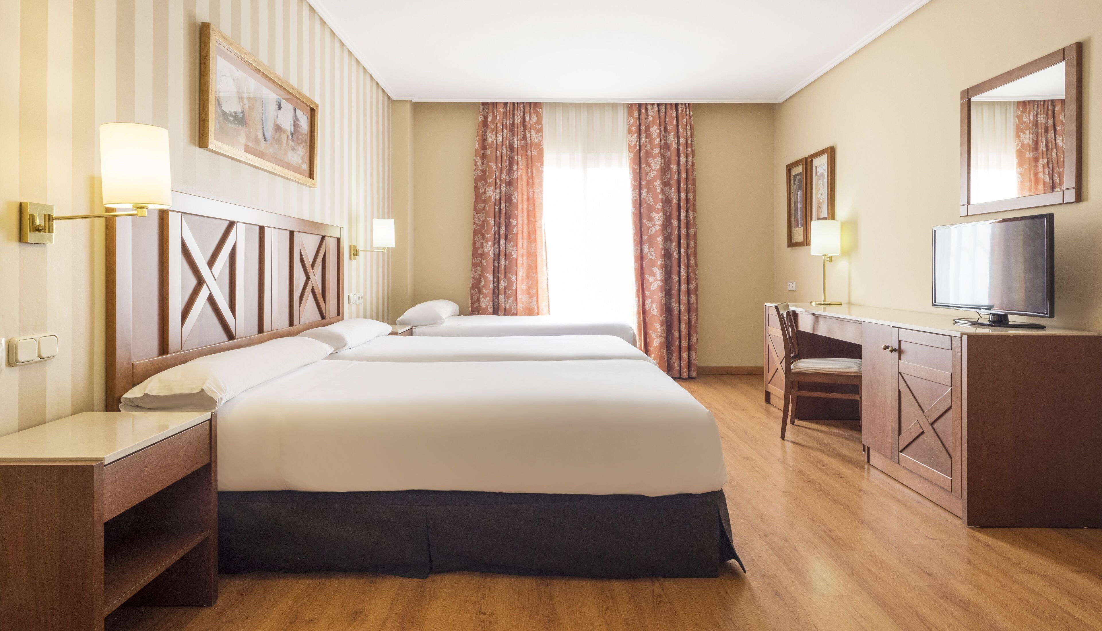 Een hotelkamer met twee bedden, een bureau, een stoel, een televisie en een groot raam met gordijnen.