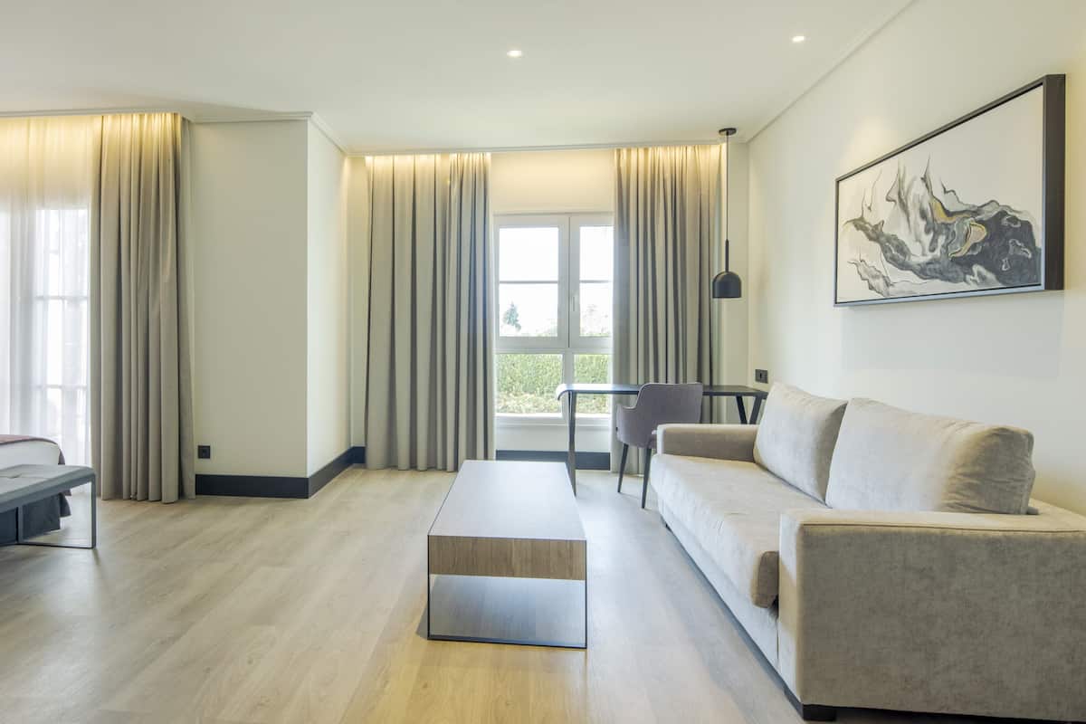 Een moderne hotelkamer met een bed, een slaapbank, een bureau en een groot raam met gordijnen.