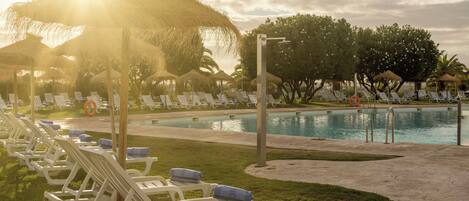 Zona de piscina con sillones de descanso y sombrillas, cielo despejado y una piscina tranquila.