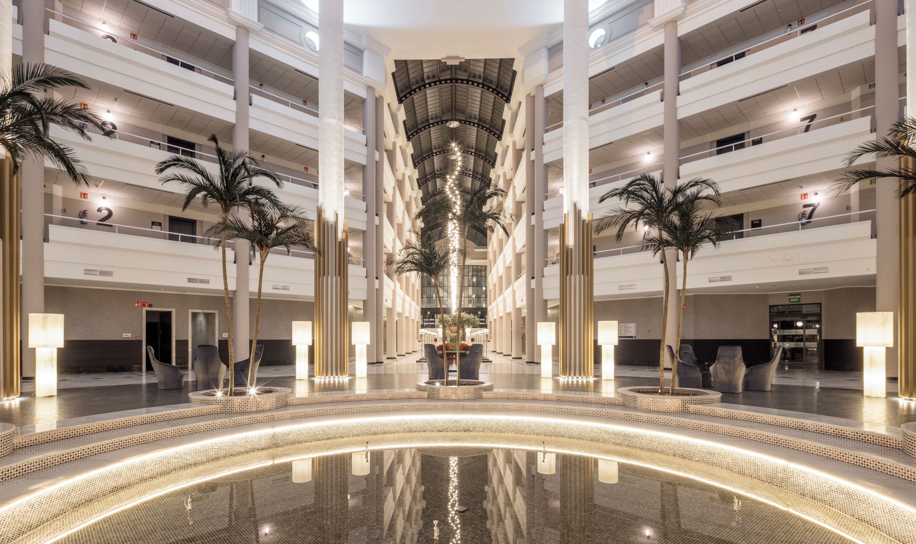 Een meerlaags atrium met een centraal waterpartij, palmbomen en een modern ontwerp.