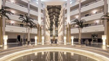 Een meerlaags atrium met een centraal waterpartij, palmbomen en een modern ontwerp.