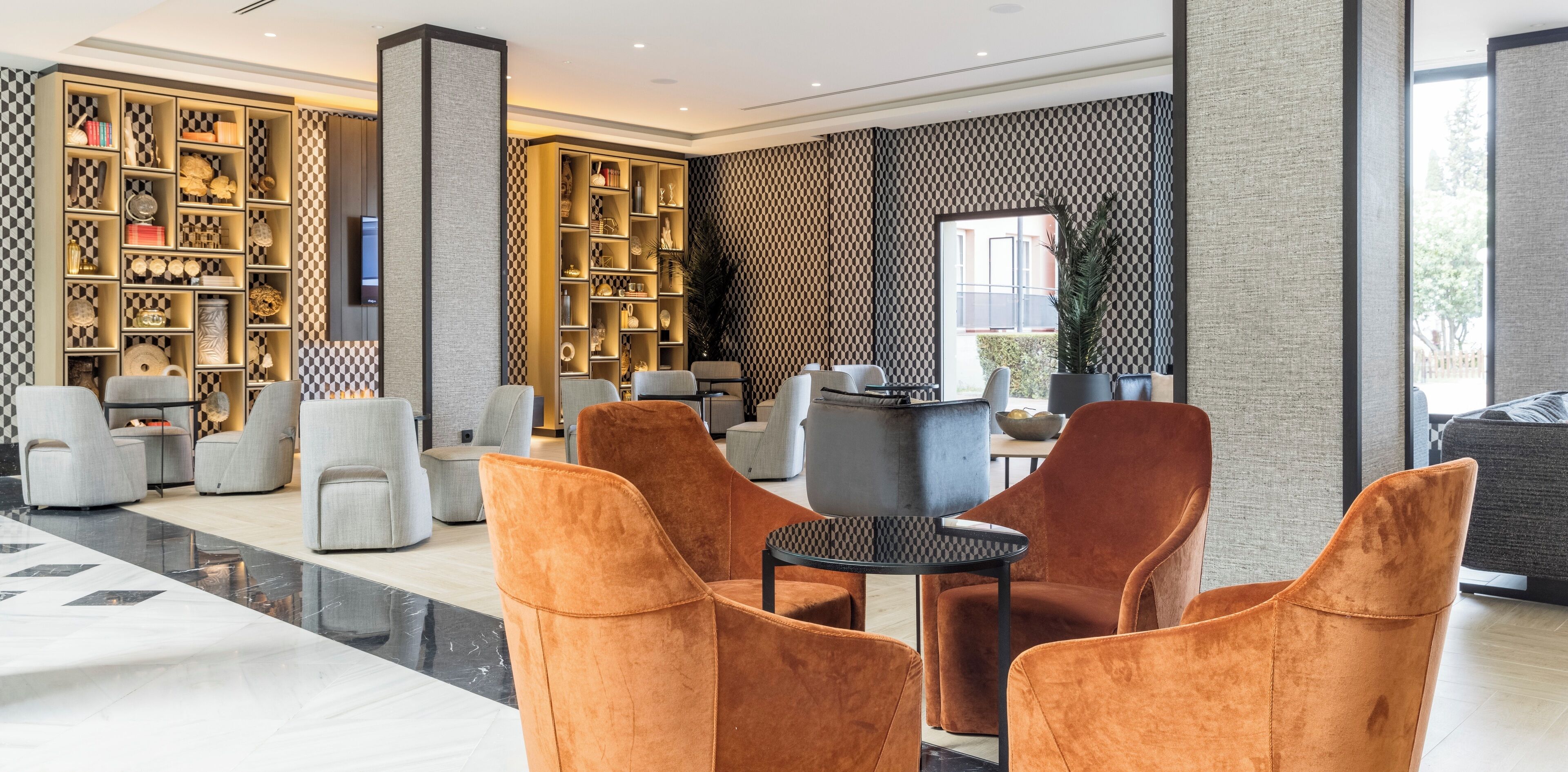 A modern lobby with a checkered wall pattern, a large bookshelf, seating area with chairs, and a reception desk.
