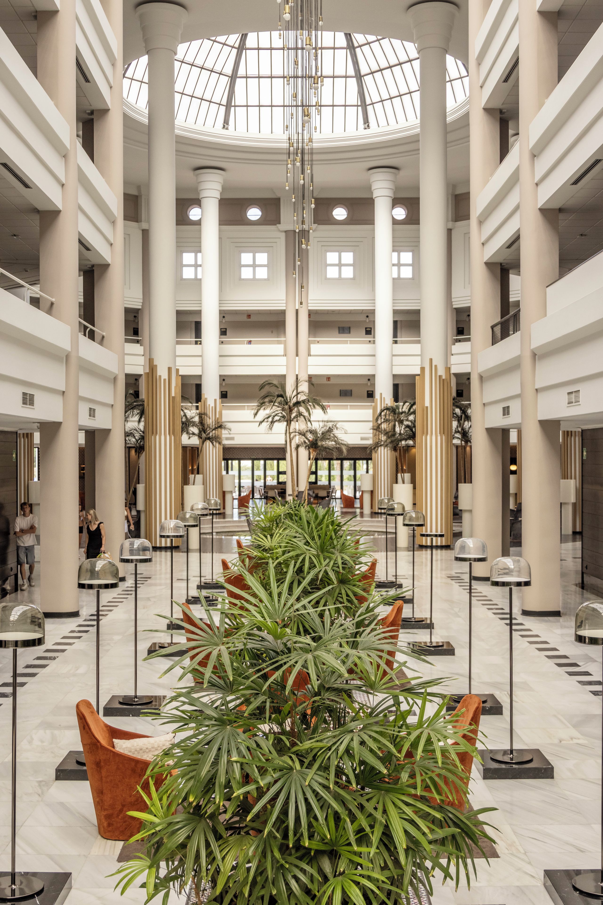 A spacious atrium with high ceilings, large columns, and a central plant arrangement.