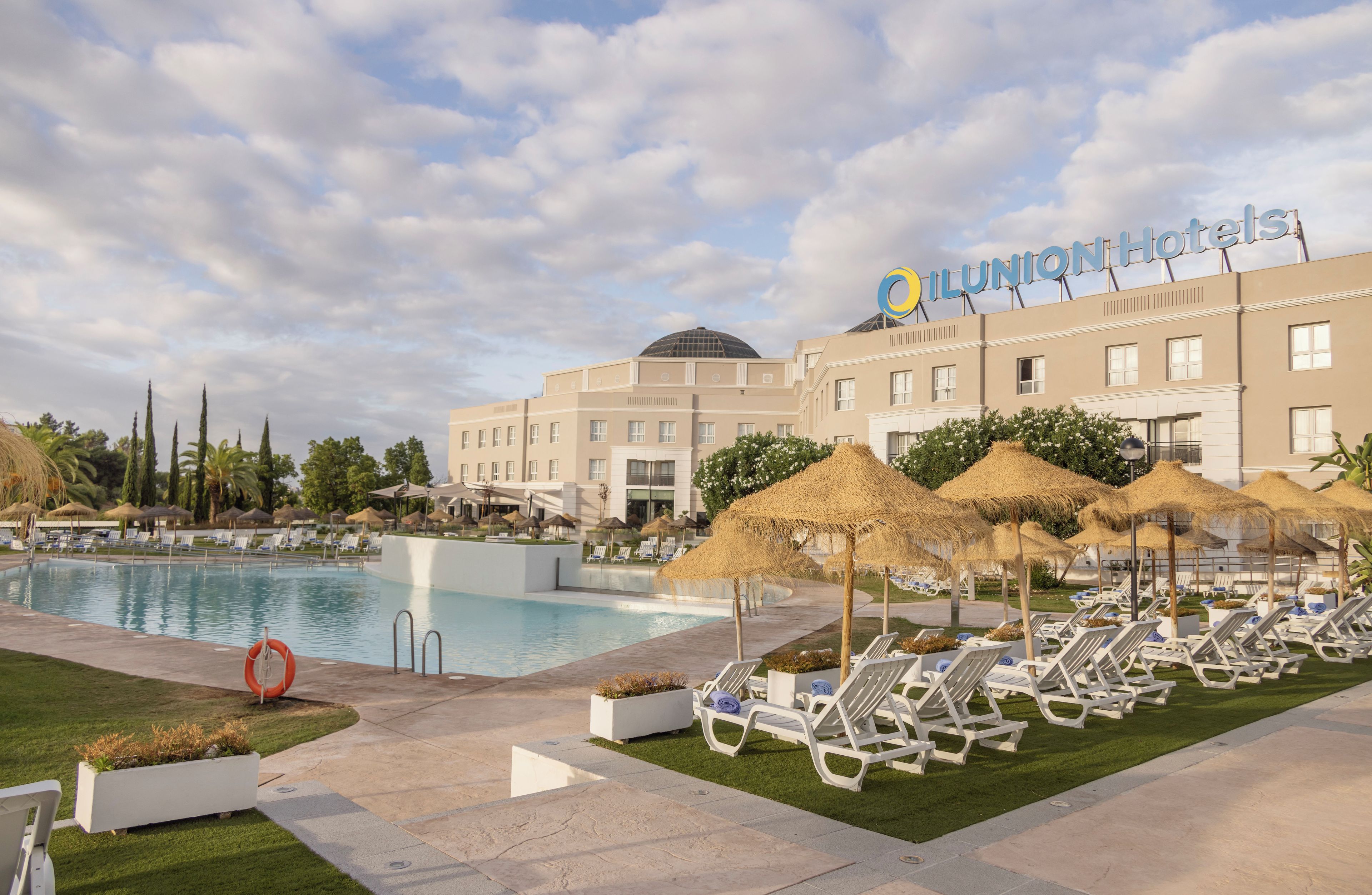A hotel with a swimming pool, lounge chairs, and umbrellas.