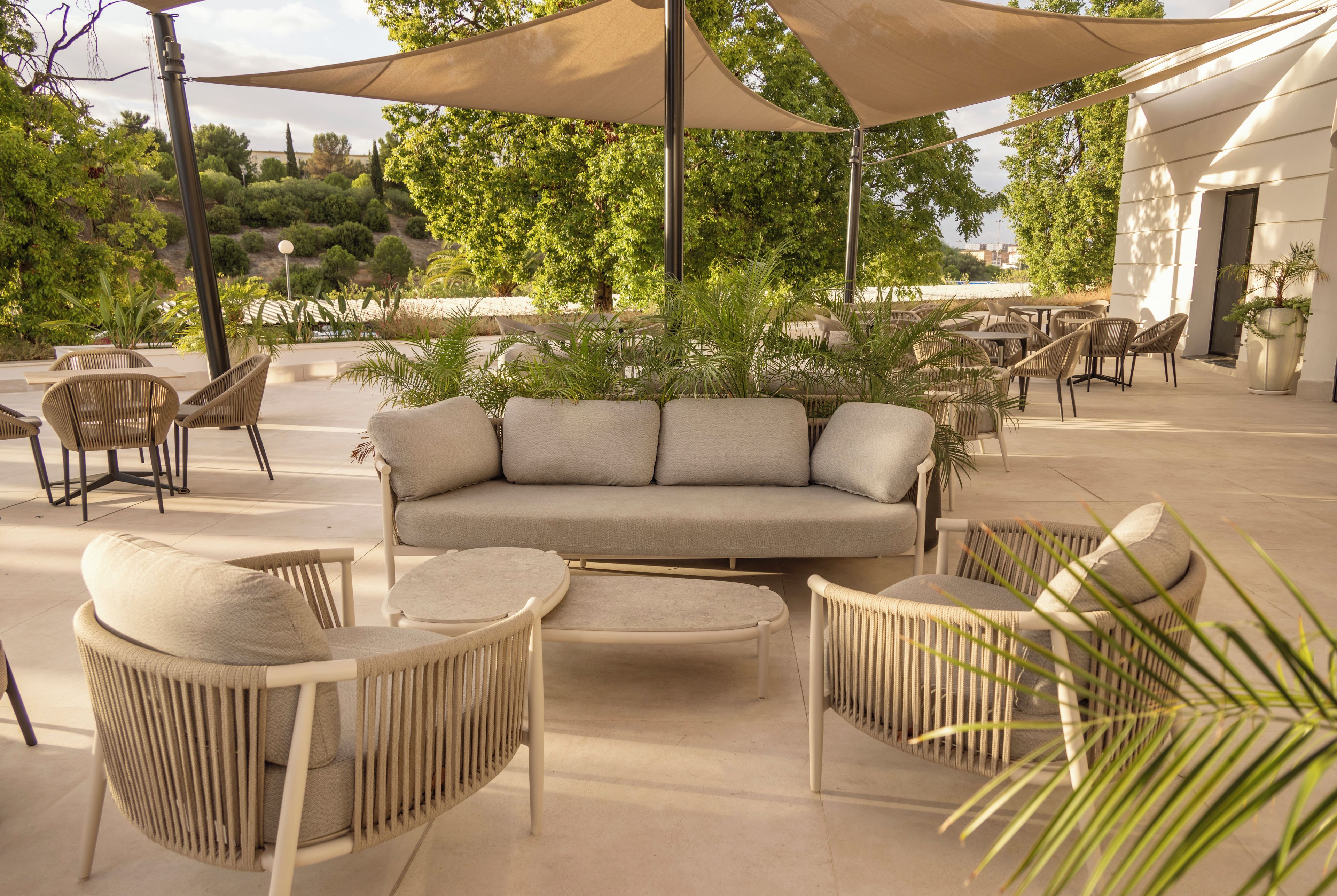 An outdoor seating area with a sofa, chairs, and tables, surrounded by plants and trees.