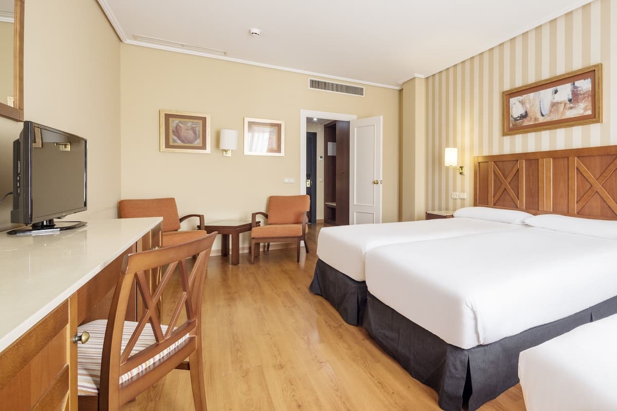 Hotelkamer met een houten bureau, twee eenpersoonsbedden, een stoel, een televisie en een deur naar een badkamer.