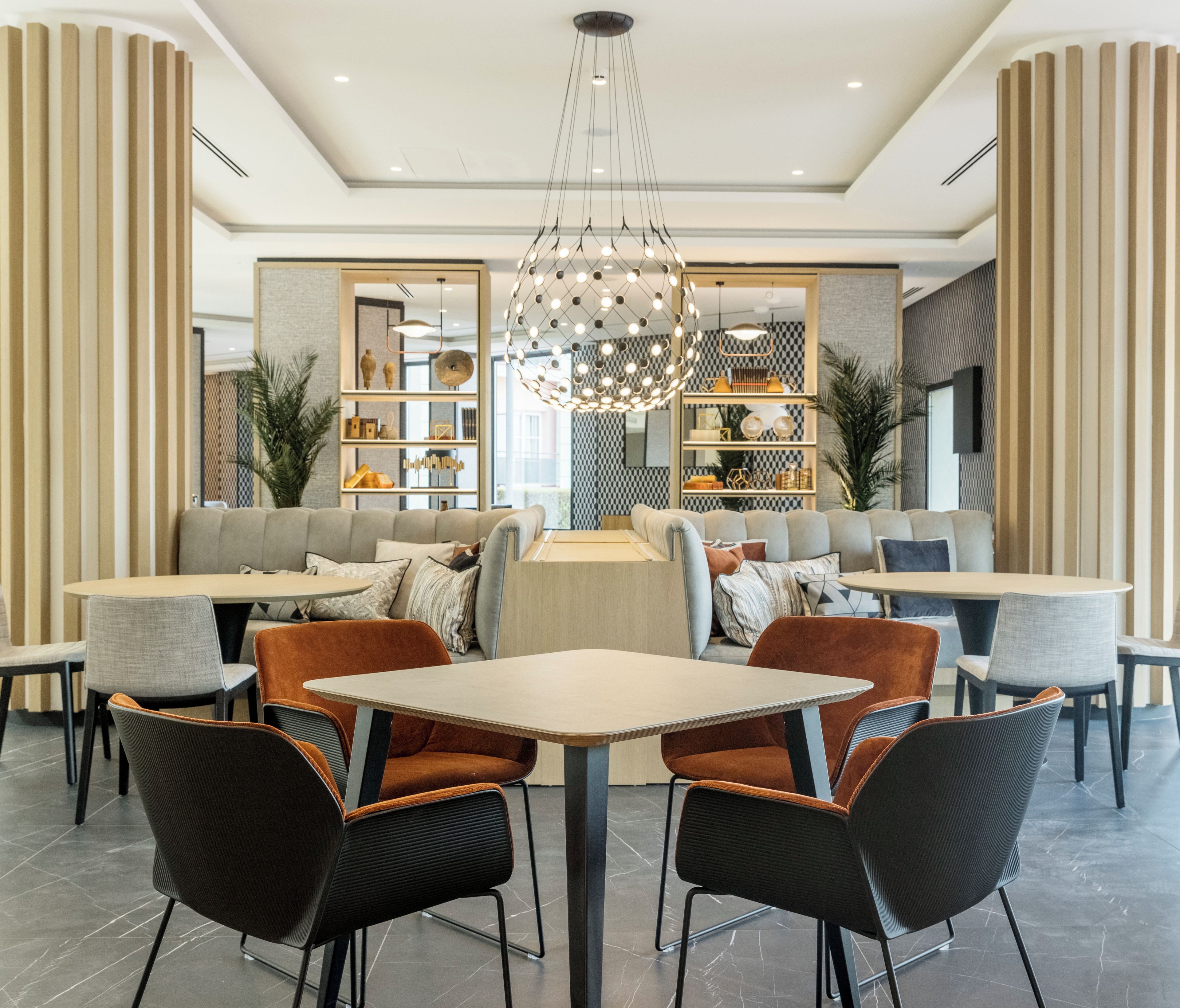 A modern dining area with round tables, cushioned seating, and a central chandelier.