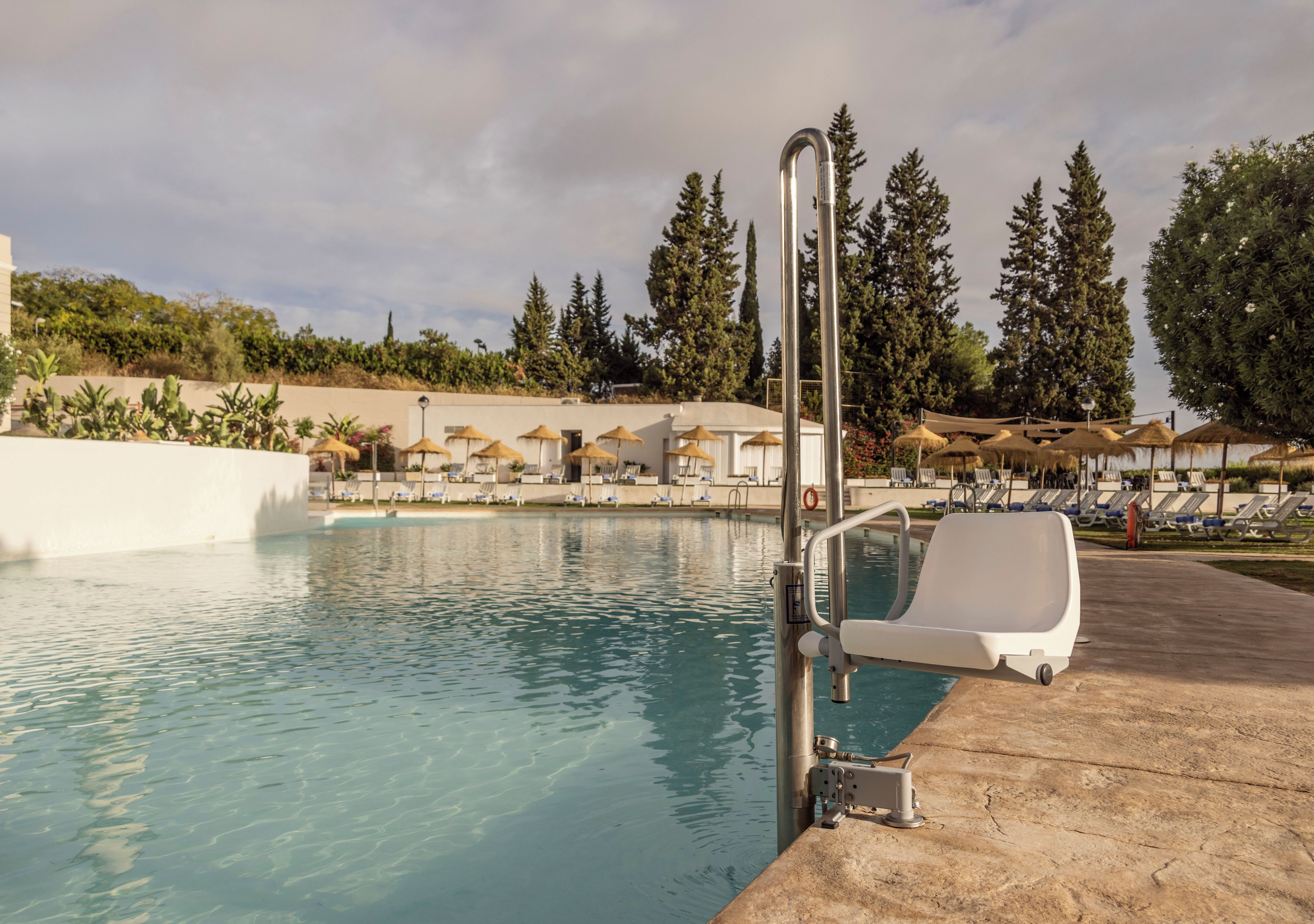 Una piscina con un puesto de salvavidas, sillas de descanso y sombrillas.