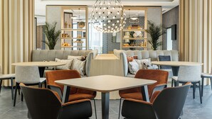 A modern dining area with a central chandelier, cushioned seating, and a mix of tables and chairs. - Hotel ILUNION Alcora Sevilla (San Juan de Aznalfarache)