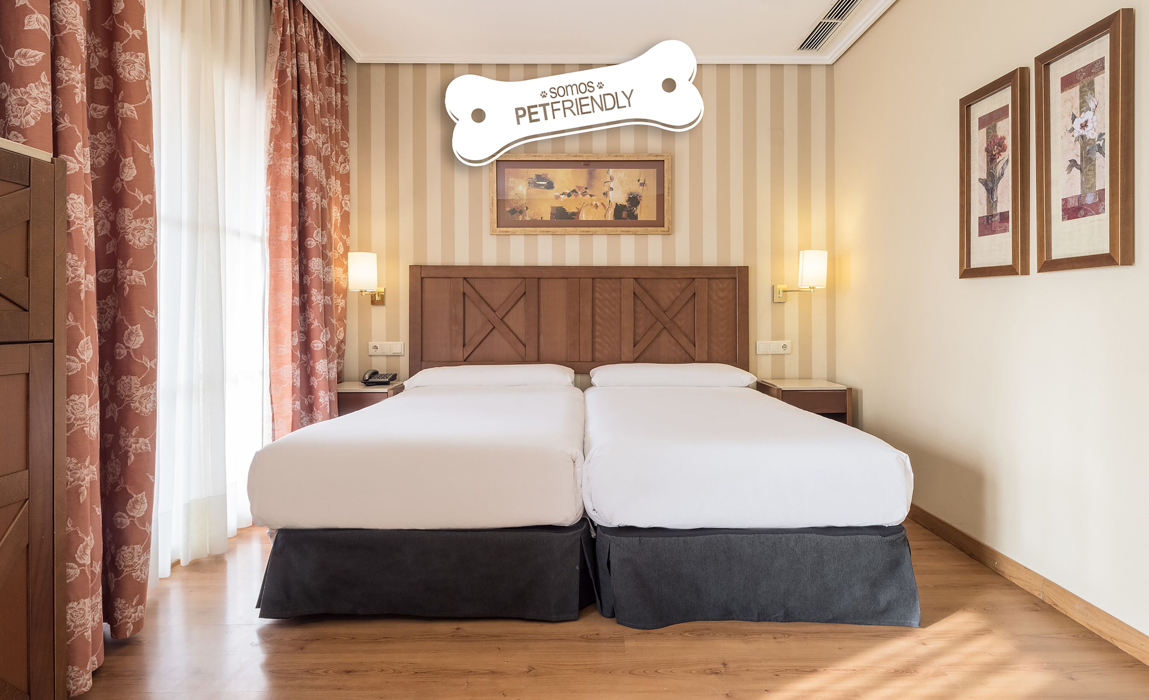Un lit double avec une tête de lit en bois, deux tables de chevet avec des lampes, un rideau à motifs floraux et une enseigne murale sur laquelle on peut lire : « Nous acceptons les animaux de compagnie ».