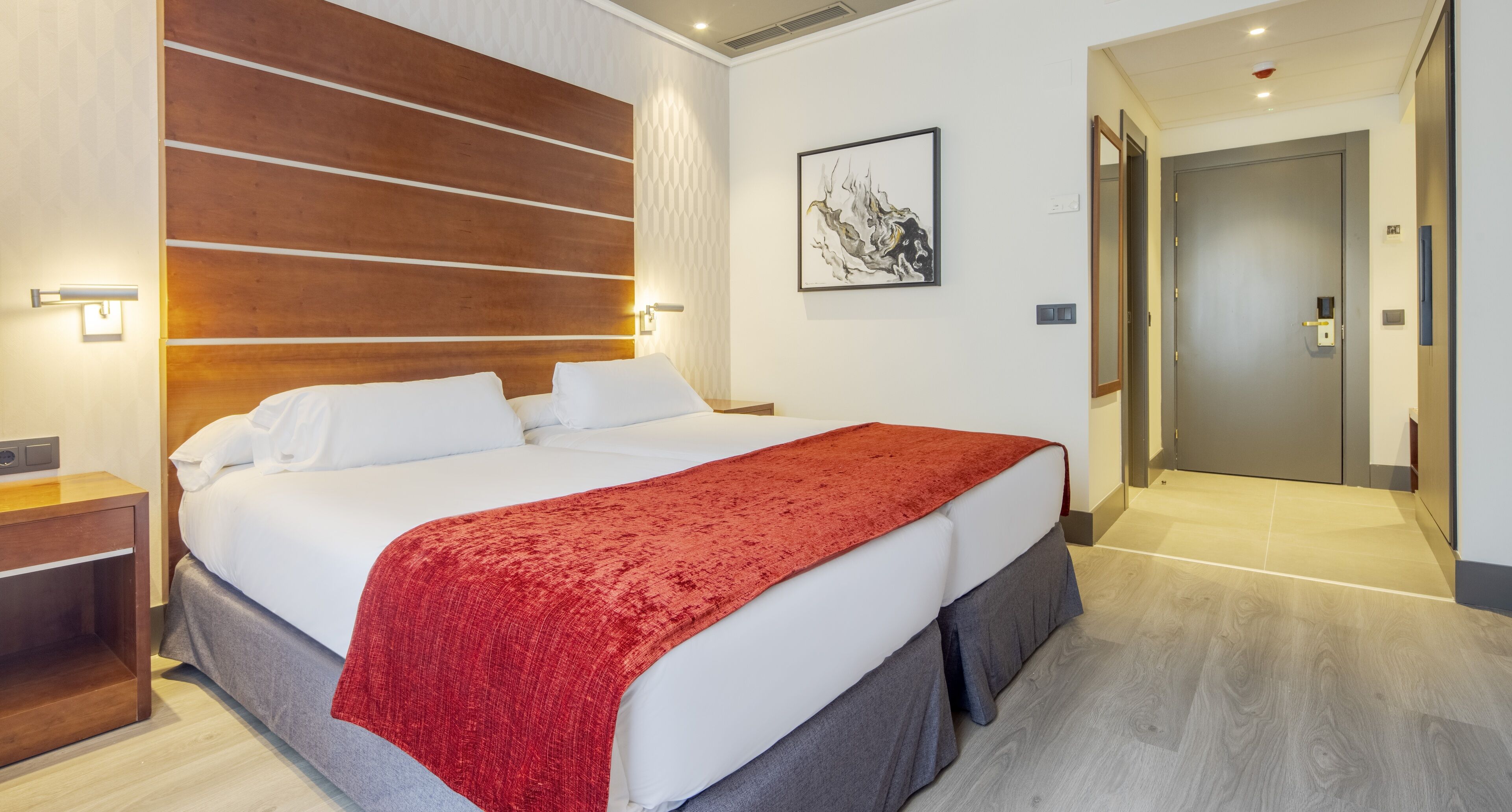 Una moderna camera d'albergo con un letto grande, una coperta rossa, una testiera in legno e un quadro appeso al muro.