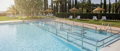 A swimming pool with clear blue water, surrounded by lounge chairs and palm trees.