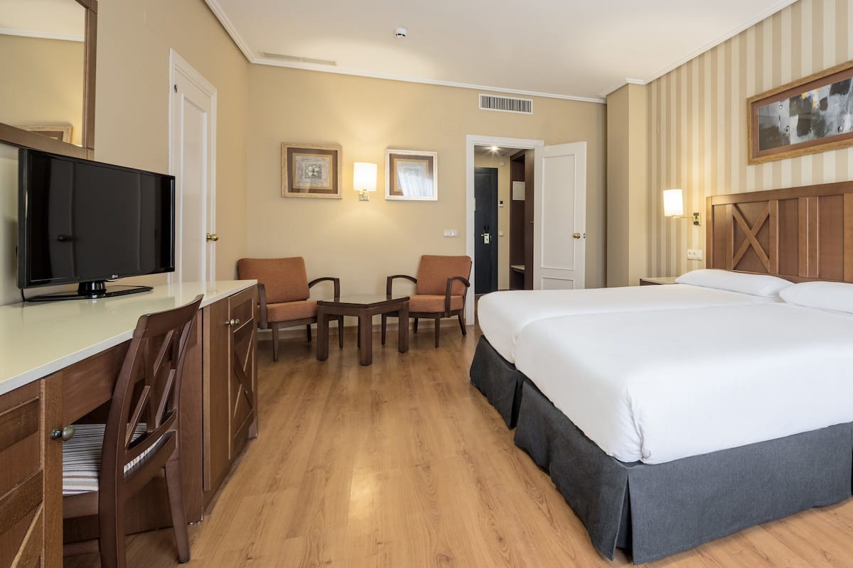 Hotelkamer met een groot bed, een bureau met een televisie, twee stoelen, een nachtkastje met een lamp en een schilderij aan de muur.