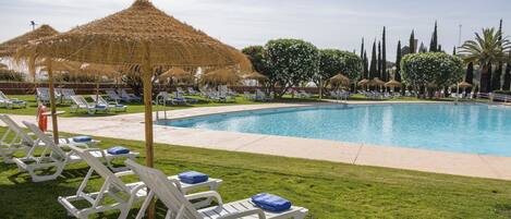 A swimming pool with sun loungers and thatched umbrellas.