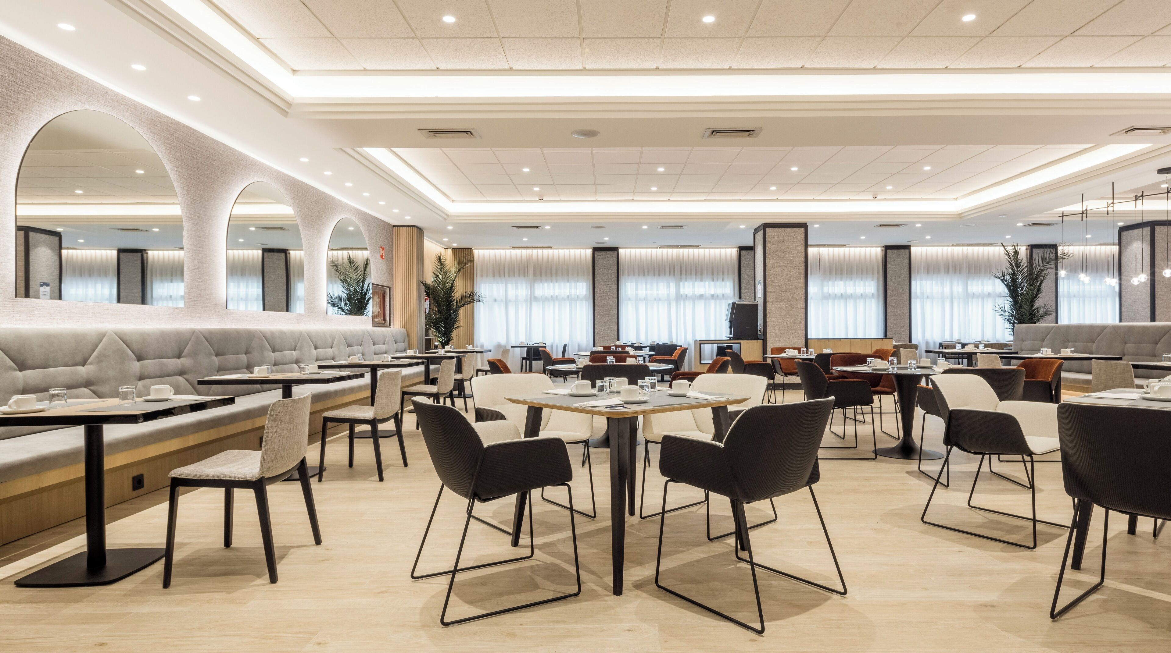 A spacious dining area with multiple seating options including booths and tables, a high ceiling with recessed lighting, and large windows with curtains.