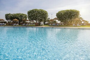 Una piscina cristalina con sillones de descanso y sombrillas al fondo.