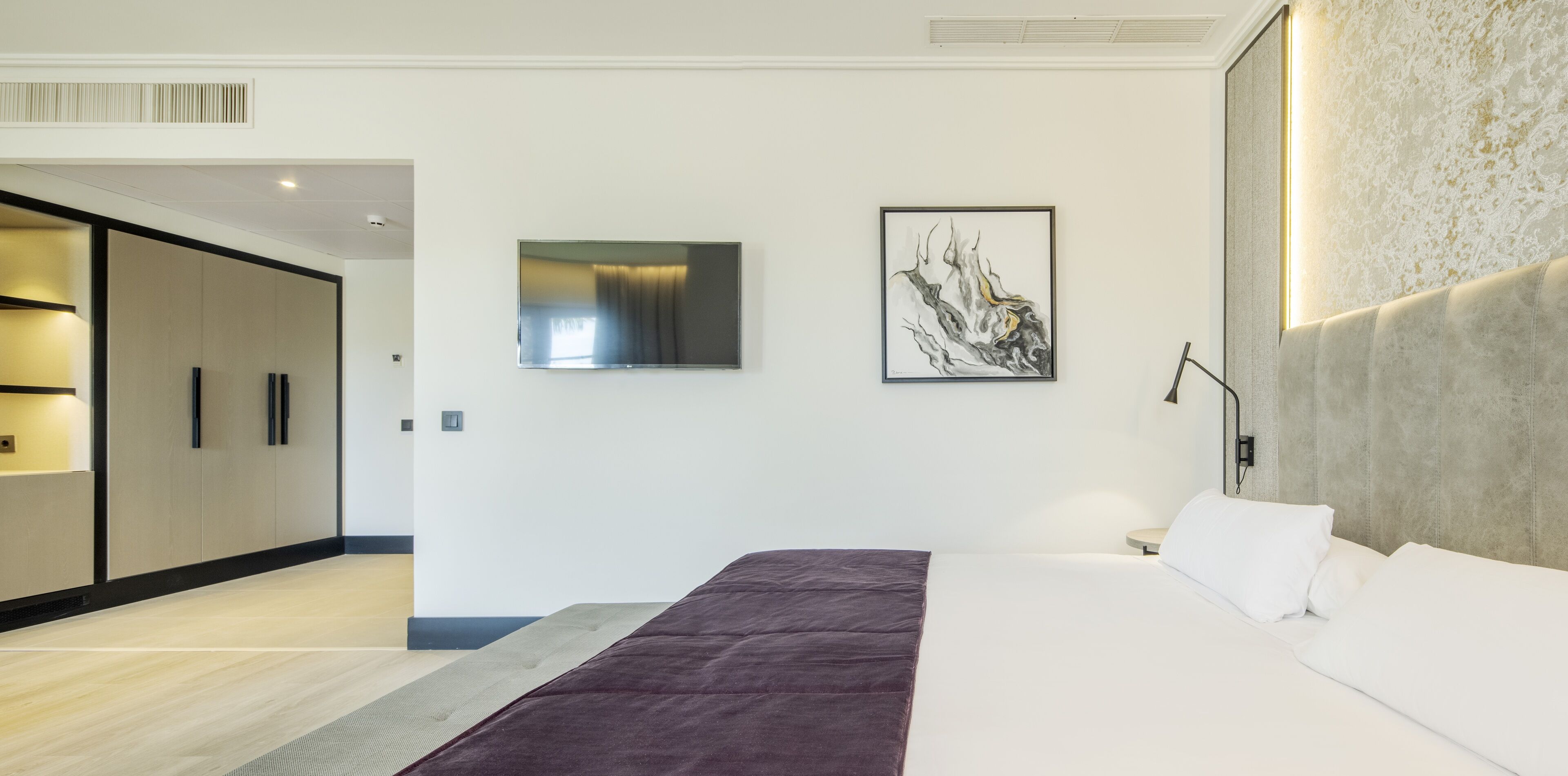 A modern hotel room with a large bed, a flat-screen TV, a painting, and a wardrobe.