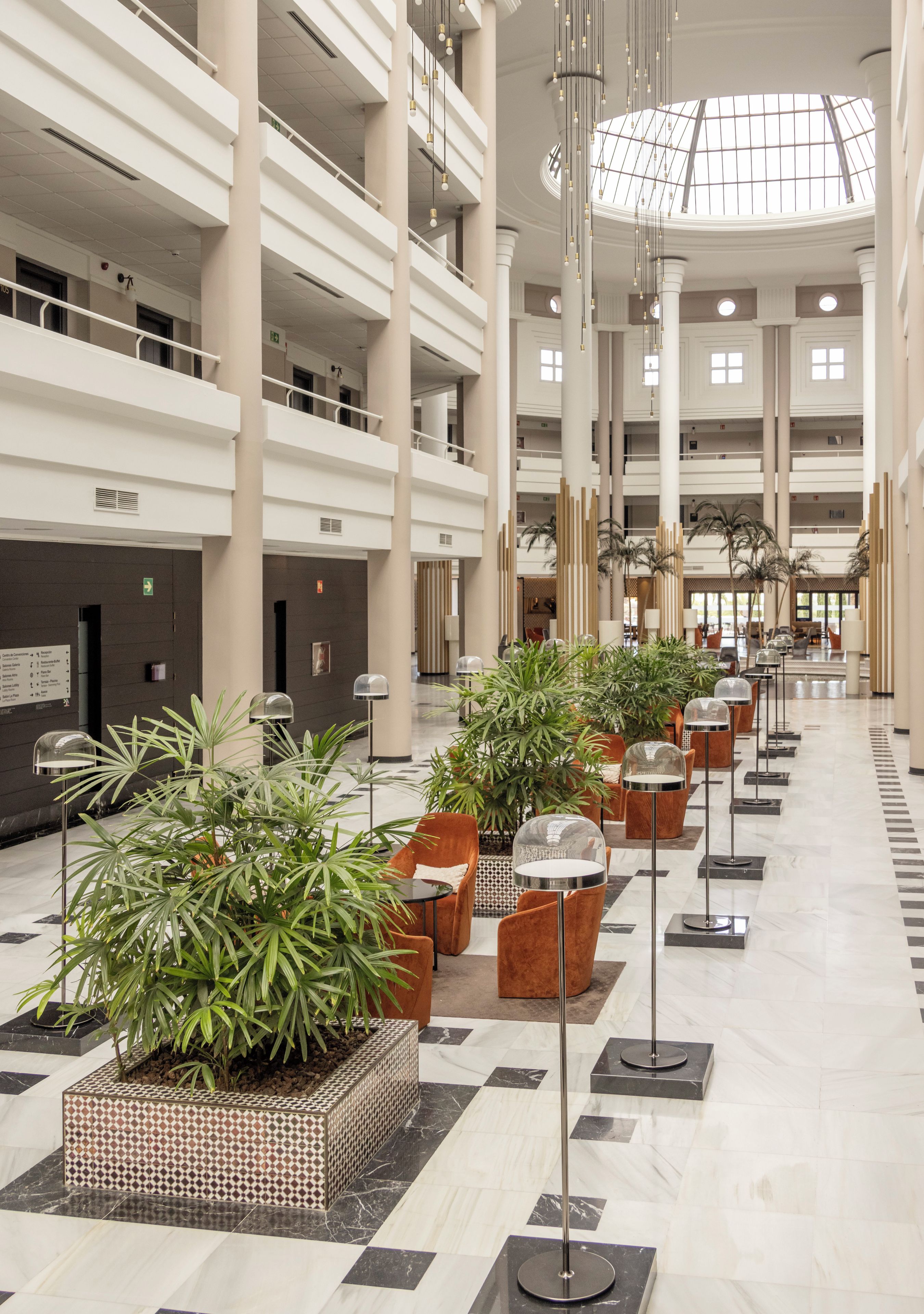 Un vestíbulo espacioso con varios pisos, grandes columnas y plantas en macetas.
