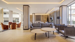 A modern lobby with a sofa set, two round tables, and a seating area with chairs. - Hotel ILUNION Alcora Sevilla (San Juan de Aznalfarache)