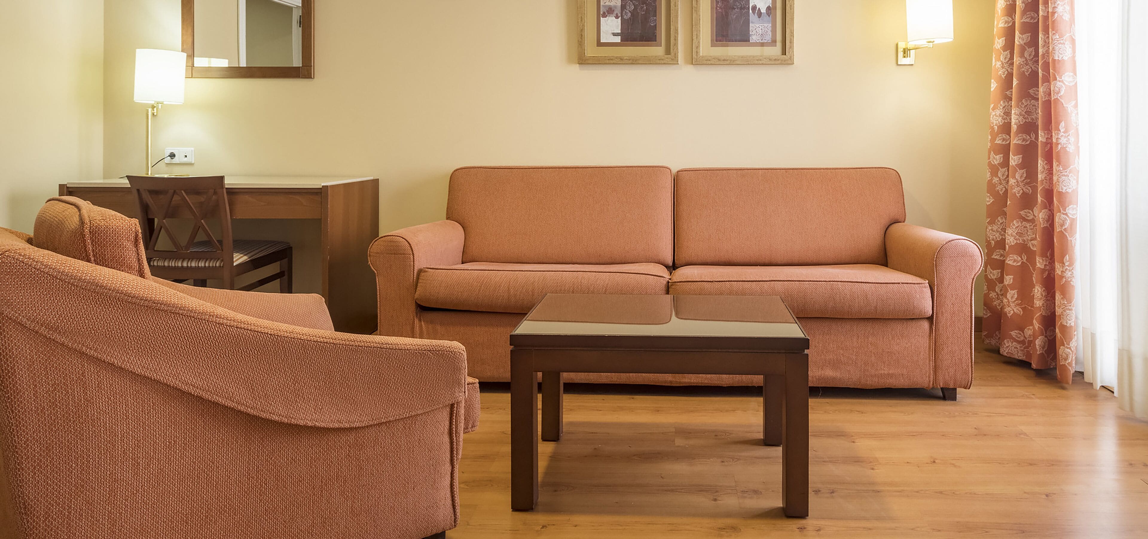 Una sala de estar con un sofá, una silla, una mesa de centro, un escritorio y una lámpara.