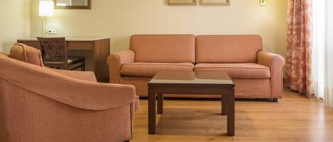 Una sala de estar con un sofá, una silla, una mesa de centro, un escritorio y una lámpara.
