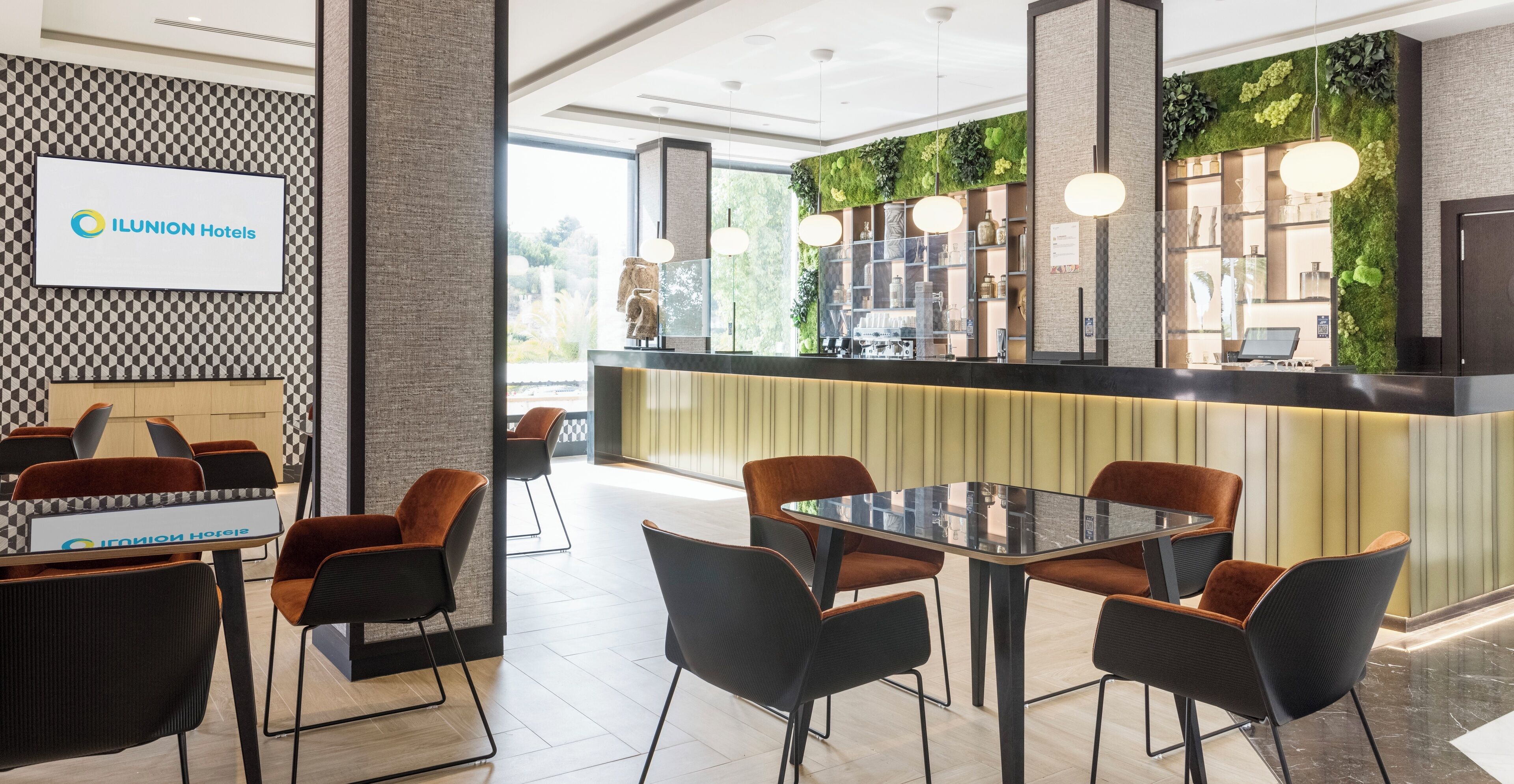 Een moderne hotellobby met een receptiebalie, een zithoek en een groene wand met planten.