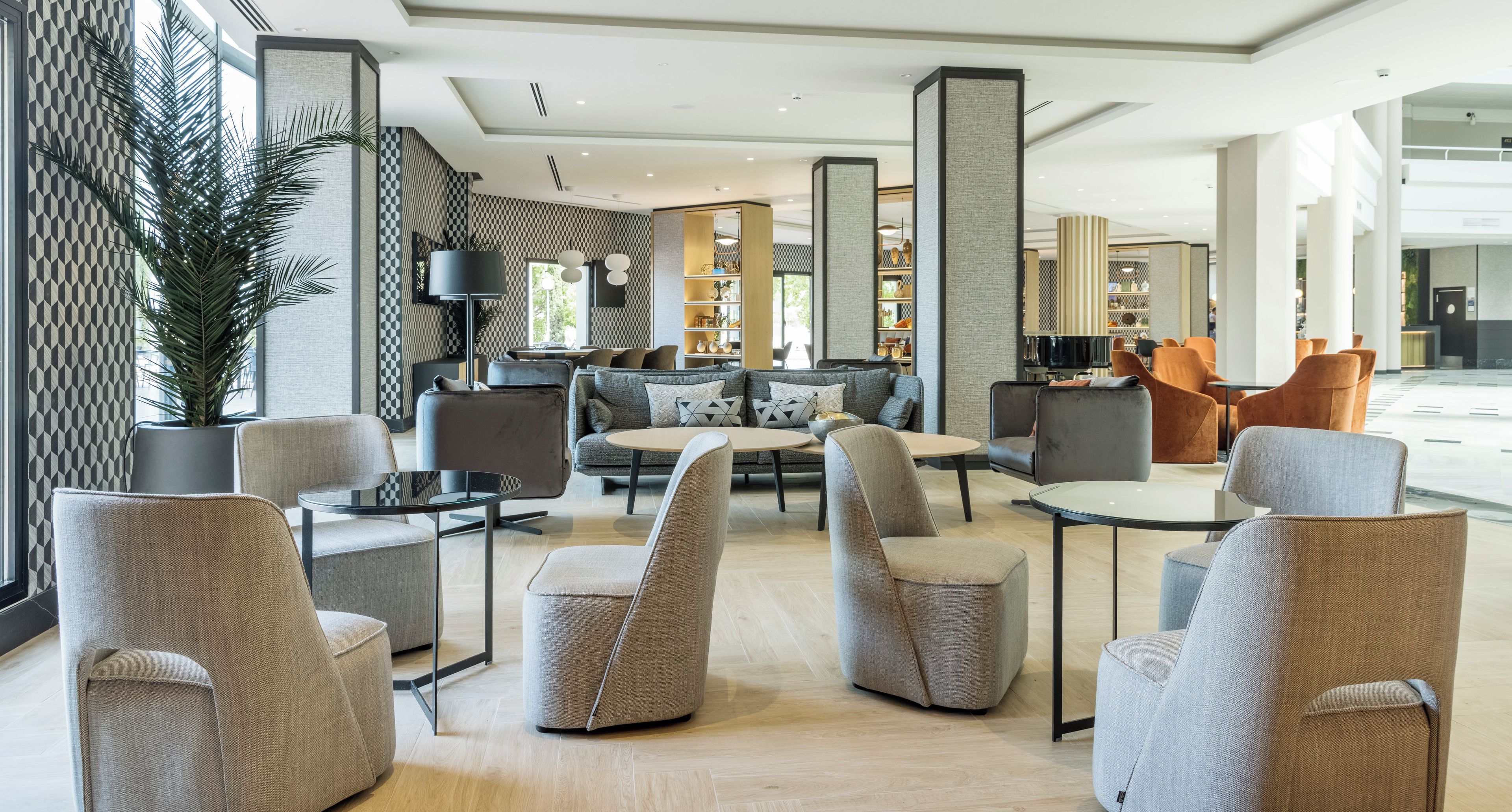 A modern lobby with seating areas, a reception desk, and a large potted plant.
