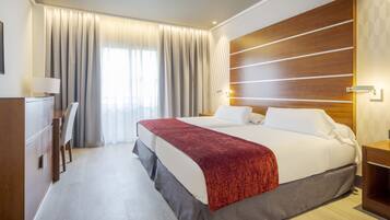 Una habitación de hotel con una cama grande, cabecera de madera, un escritorio y una silla.
