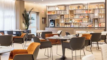 A modern dining area with round tables and chairs, a coffee machine, and a wall of shelves with various items.