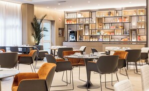 Un área de comedor moderna con mesas y sillas redondas, una máquina de café y una estantería con diversos objetos.