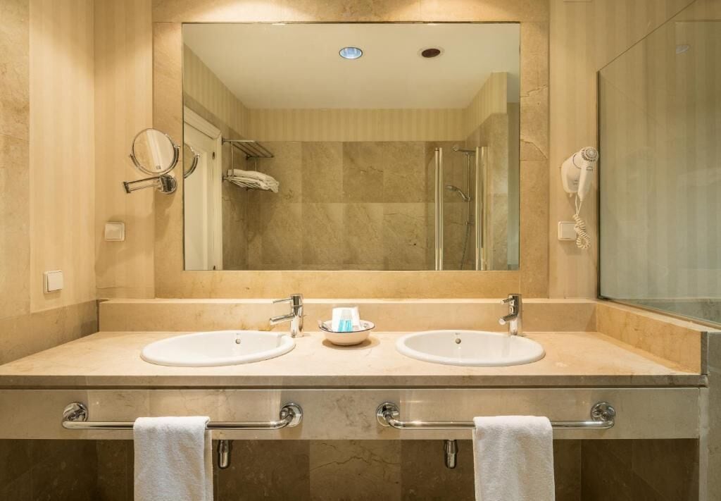 Un baño moderno con dos lavamanos, un espejo grande, un perchero para toallas y un secador de pelo.