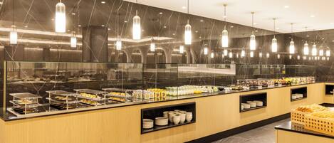 A buffet area with a marble backsplash, hanging pendant lights, and a variety of food items displayed on shelves.