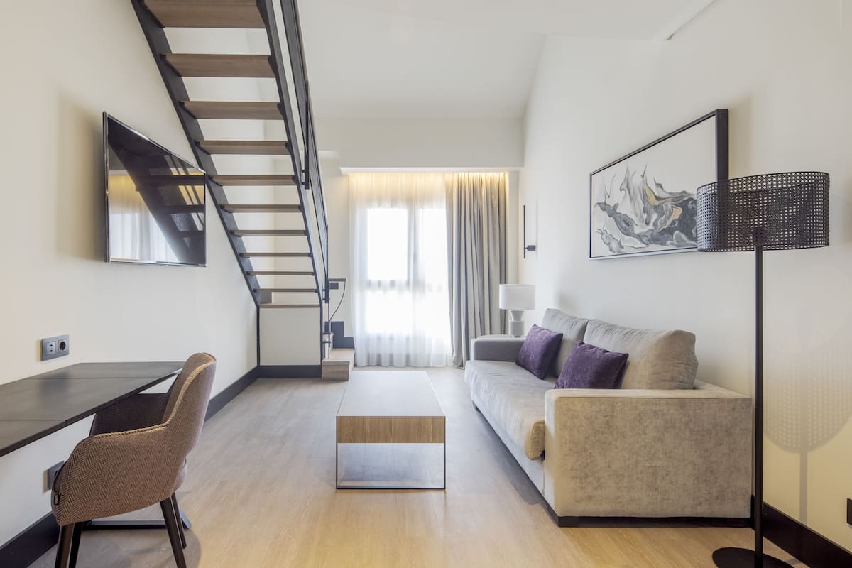 Een moderne woonkamer met een bank, een salontafel, een aan de muur bevestigde televisie, een trap en een vloerlamp.