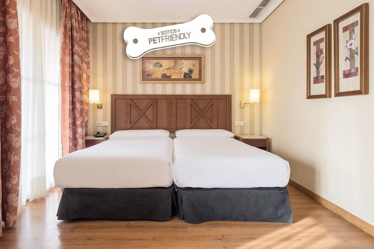 Un lit double avec une tête de lit en bois, deux tables de chevet avec des lampes, une inscription au-dessus du lit et un tableau encadré au mur.