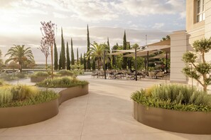 Un espace extérieur aménagé avec des tables et des chaises, entouré de jardinières et d’arbres.
