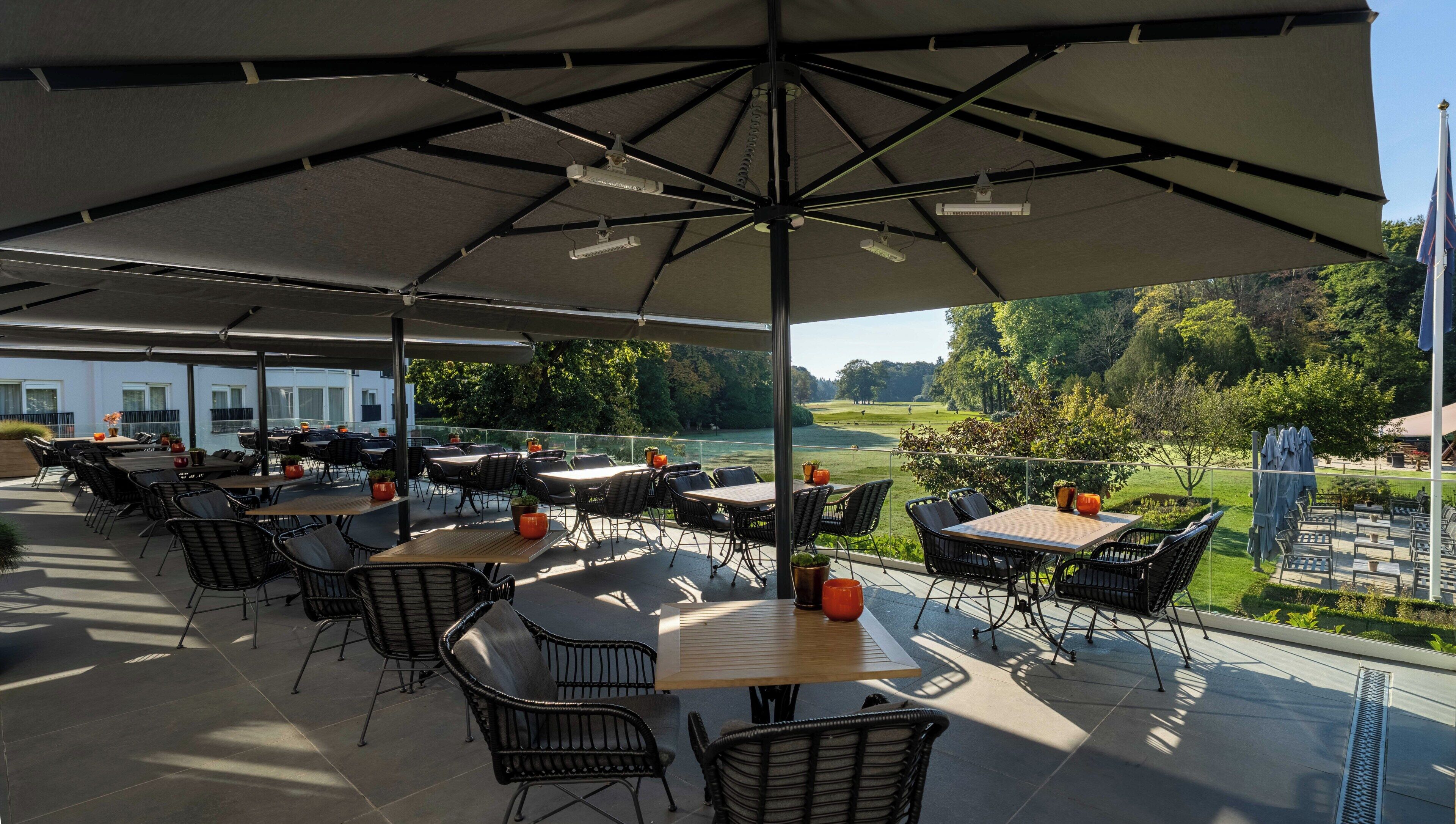 An outdoor patio with tables and chairs, a large umbrella, and a view of a golf course.