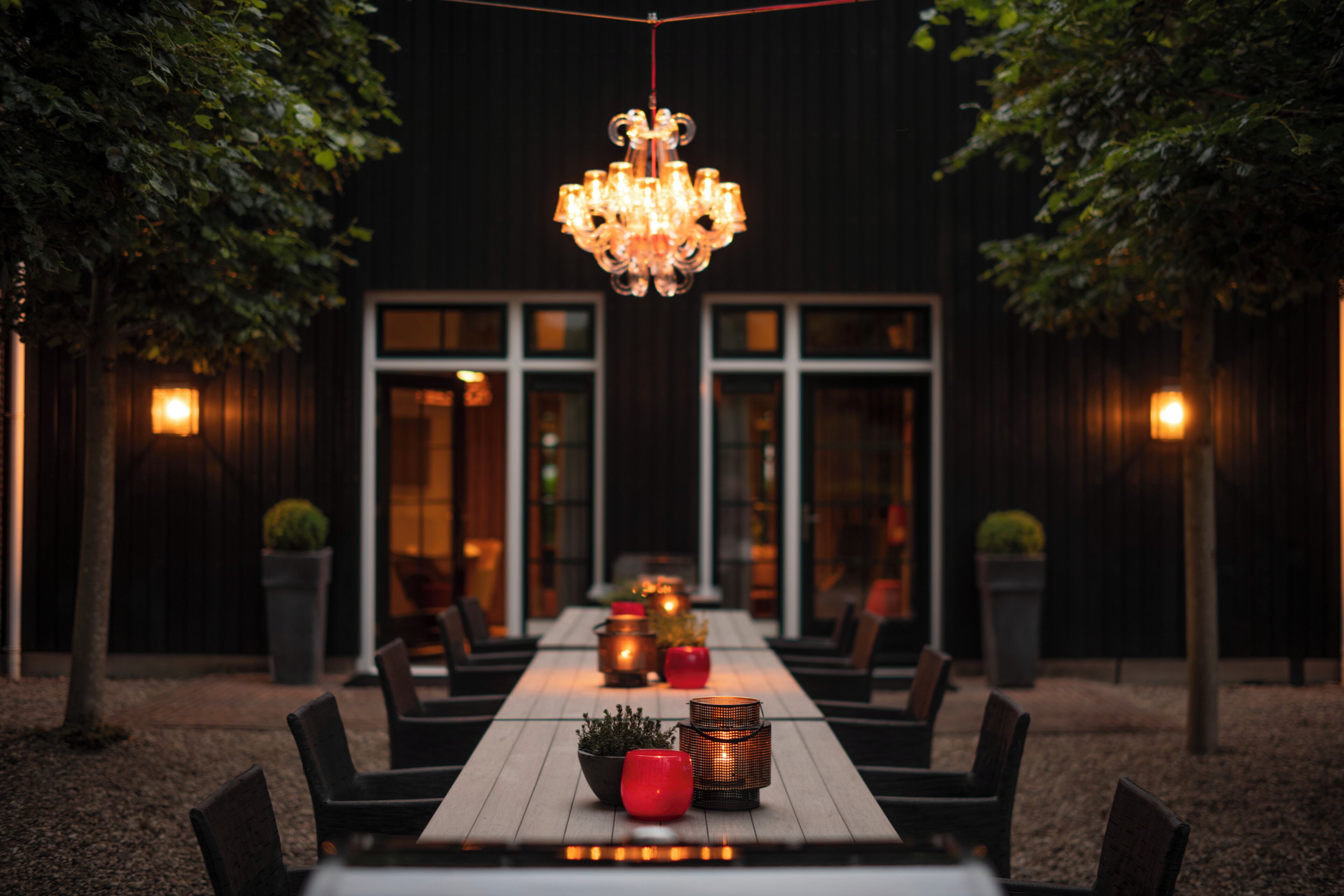 An outdoor dining area with a long table, chairs, and a chandelier.