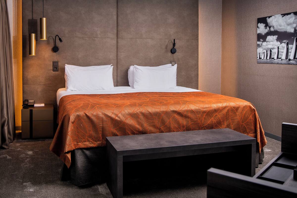 A modern hotel room with a large bed, a bench, and a nightstand.