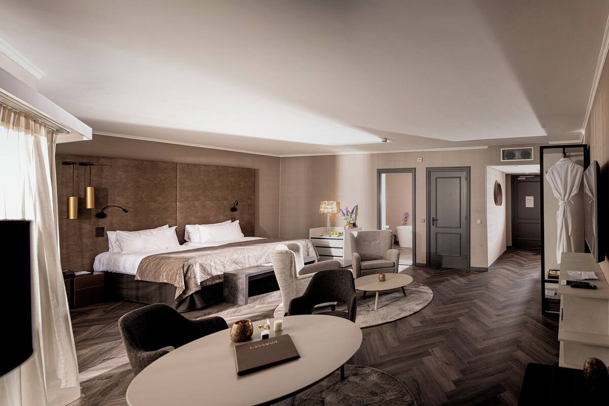 A hotel room with a bed, a desk, a chair, a round table, and a large mirror.