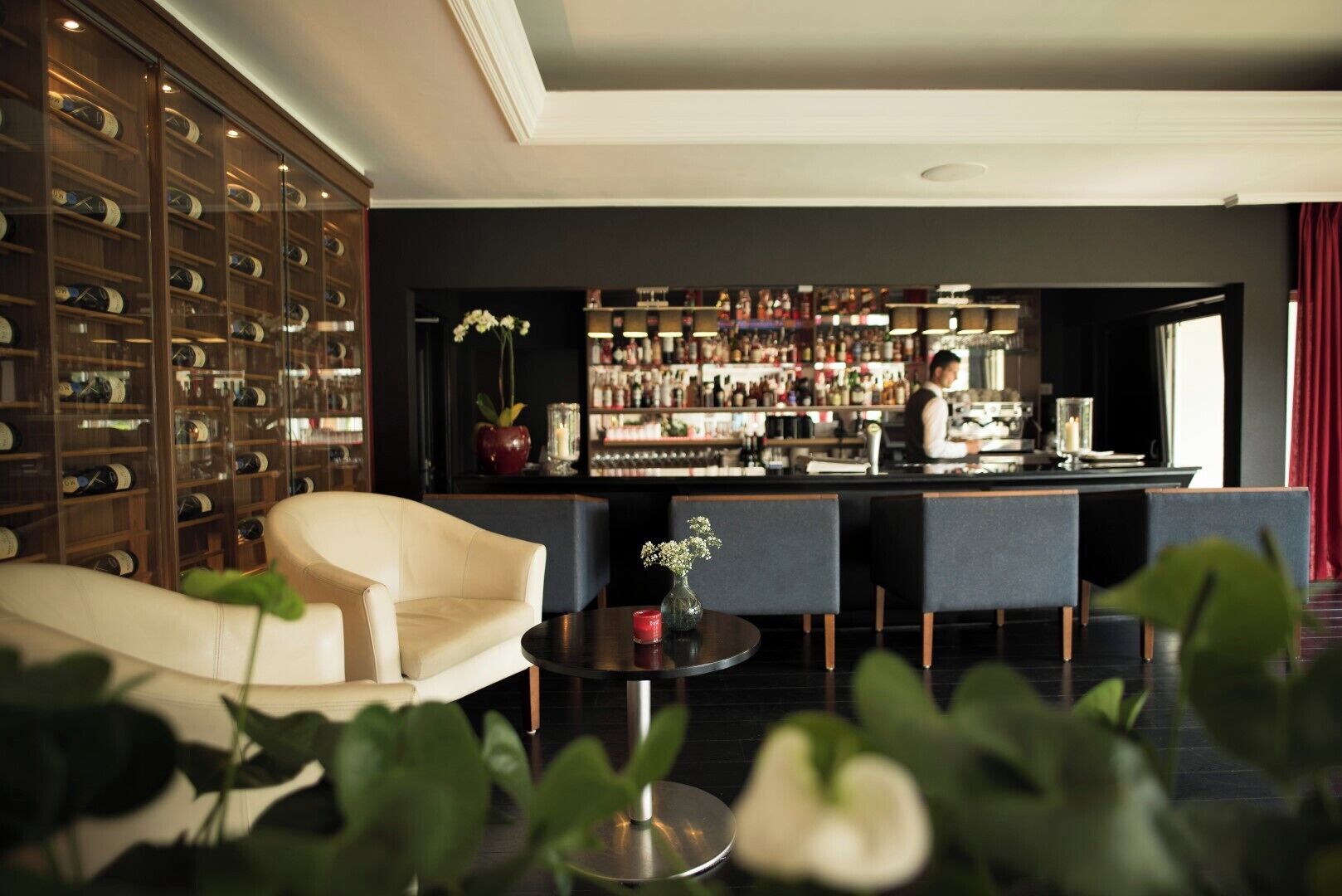A bar area with a bartender, a wine rack, and seating.