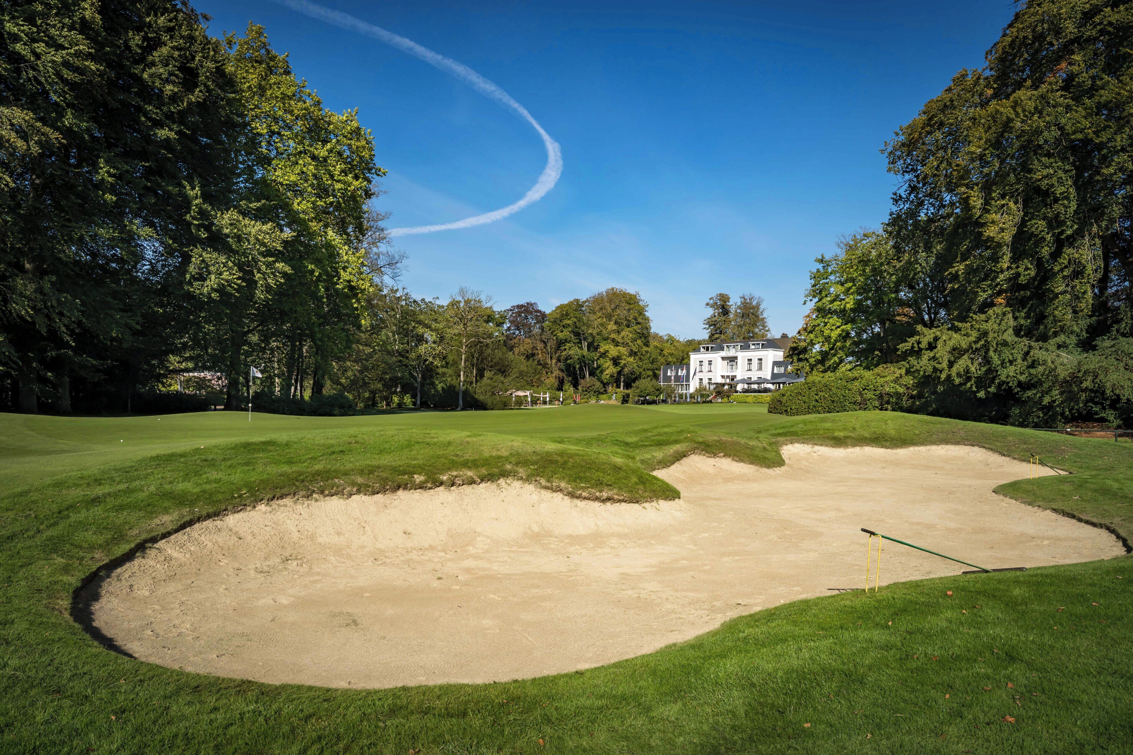 Un campo de golf con búnkeres, un marcador de bandera y un edificio grande al fondo.