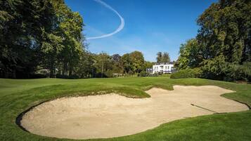 Un campo de golf con búnkeres, un marcador de bandera y un edificio grande al fondo.