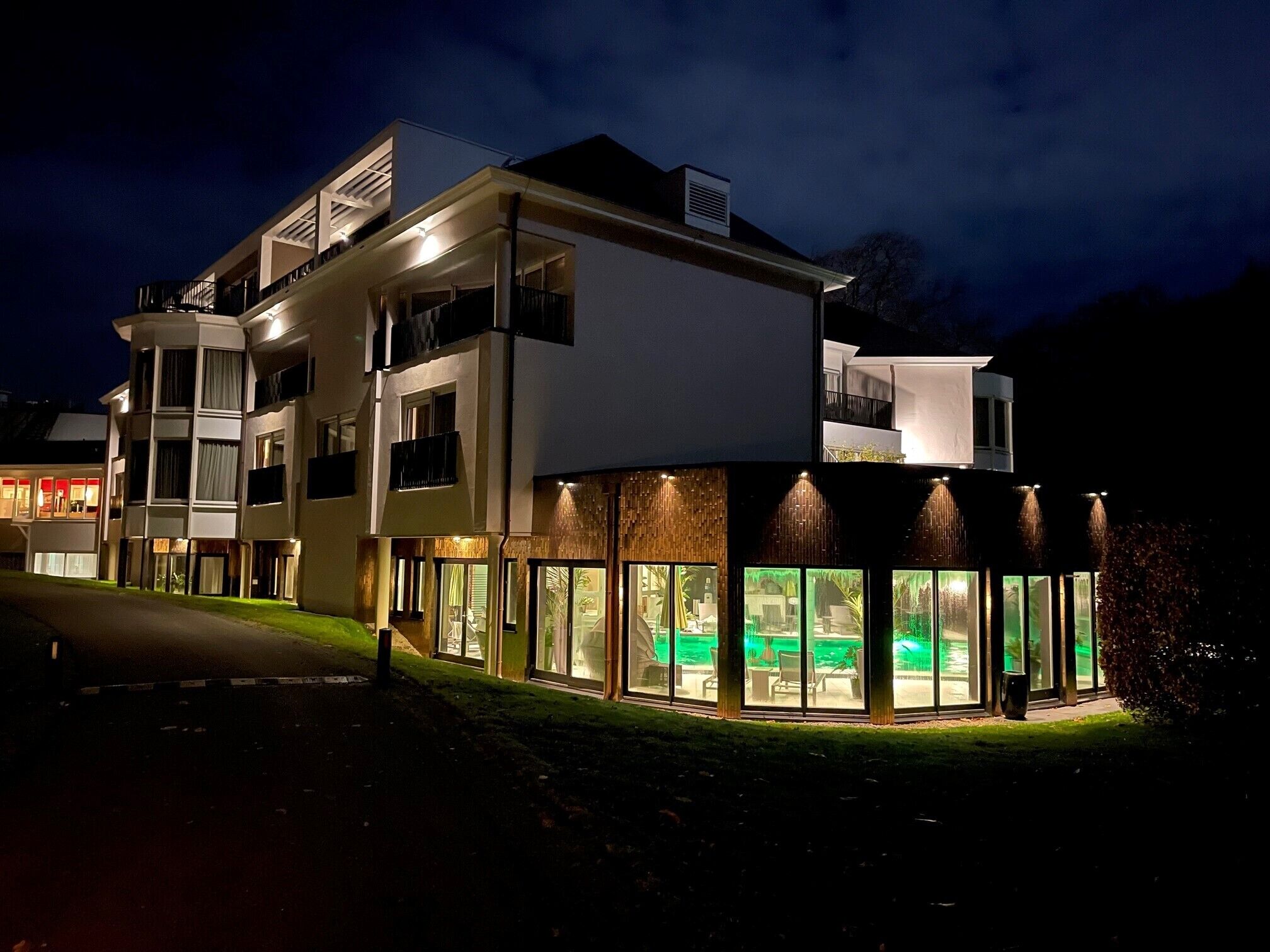 A modern multi-story hotel with a curved glass facade, outdoor seating area, and a well-lit entrance.