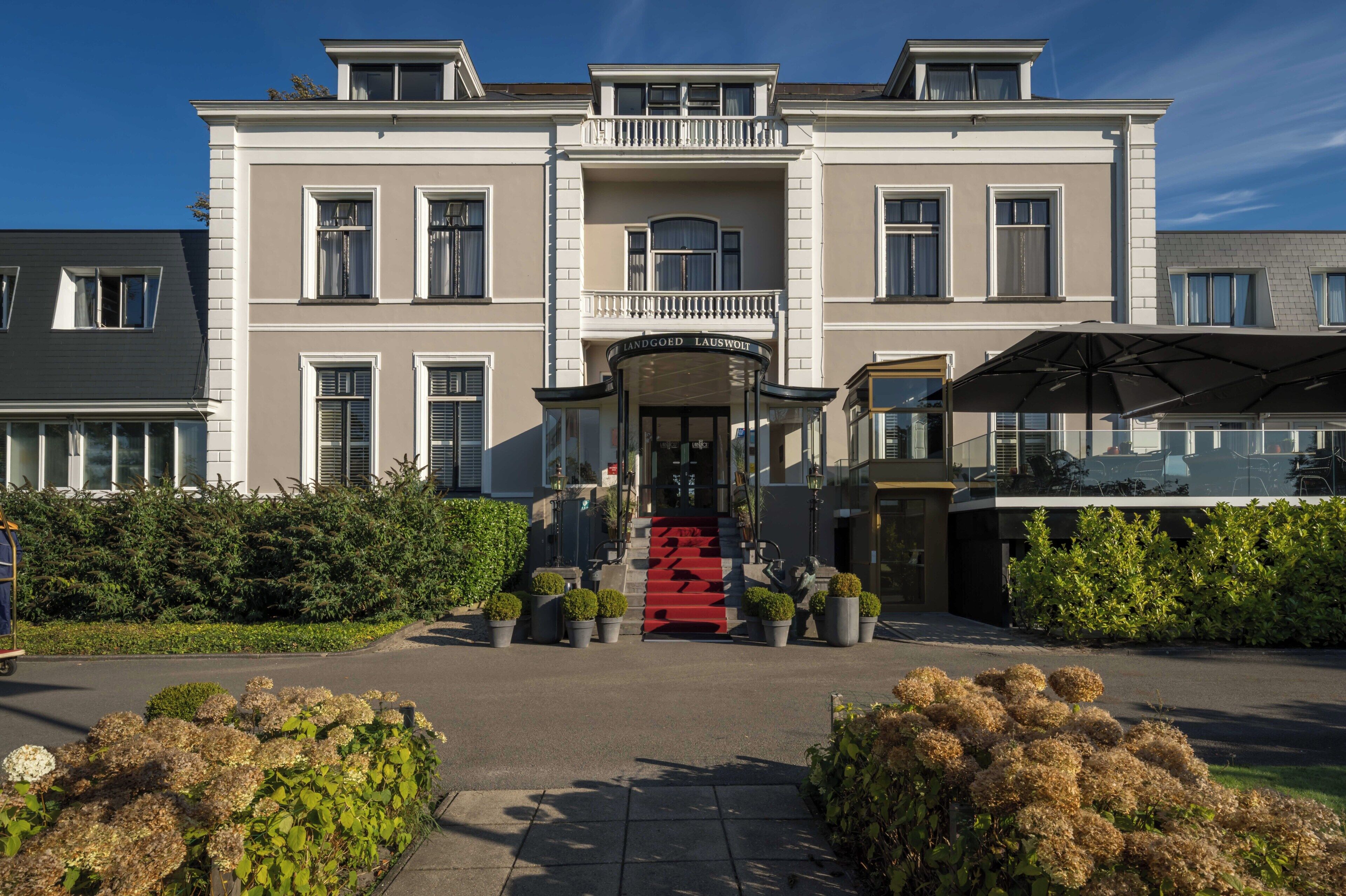 A large, two-story building with a central entrance, a balcony, and a covered area with outdoor seating.