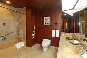 Un baño con bañera, inodoro, lavamanos y un espejo grande.