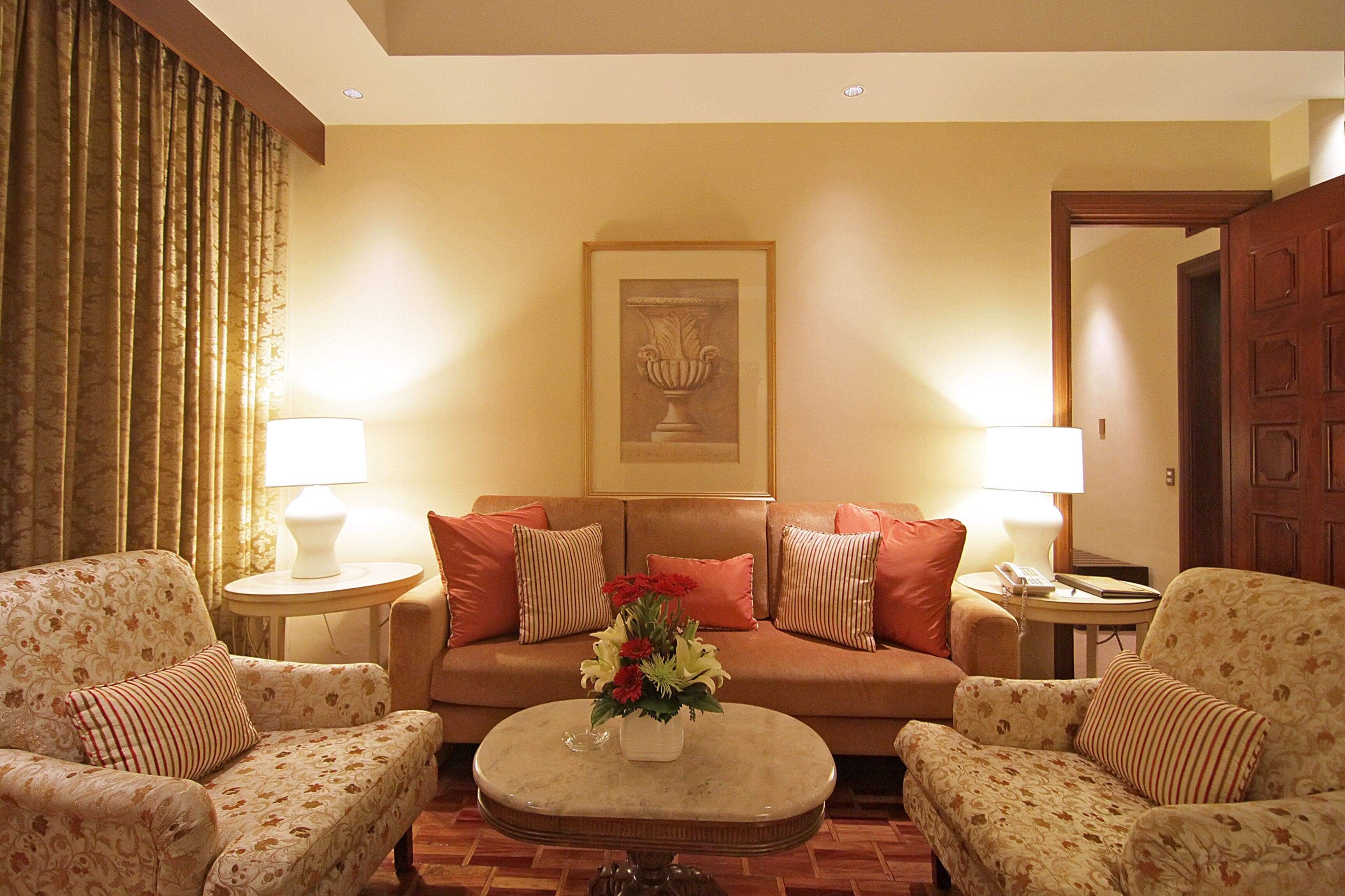 A living room with a sofa, two armchairs, a coffee table with a floral arrangement, and two lamps.