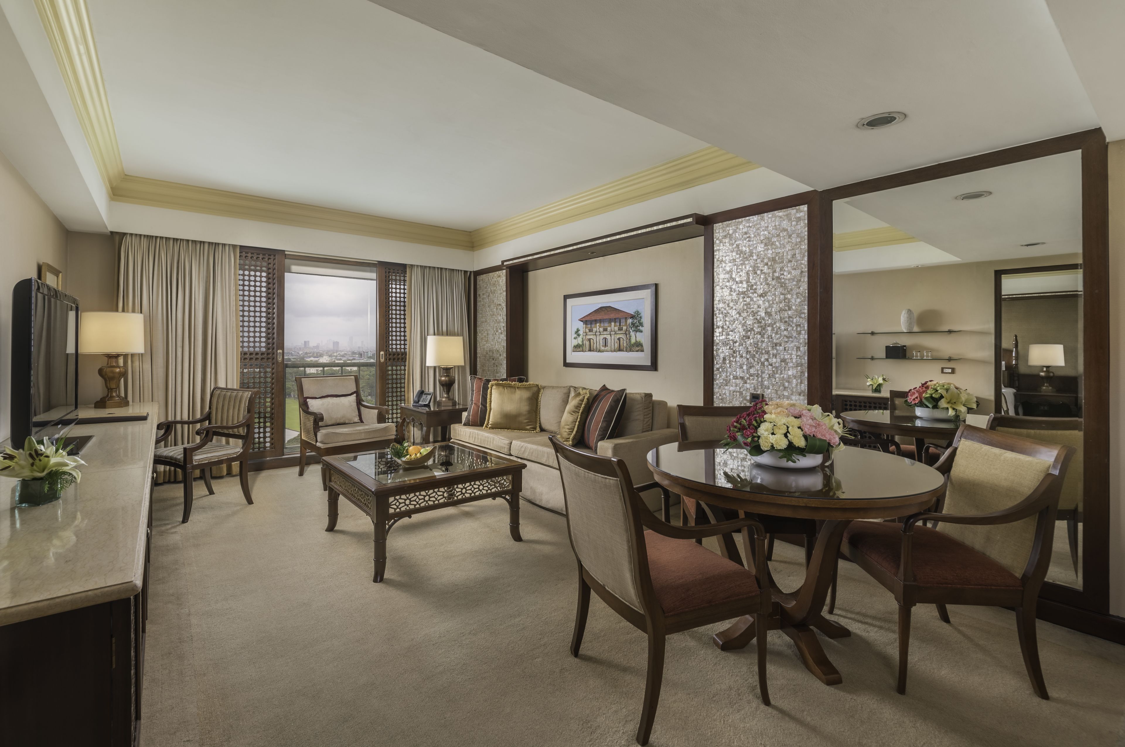 A hotel room with a living area, dining table, and a view of the city.
